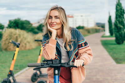 A young smiling woman rides a rented electric scooter.