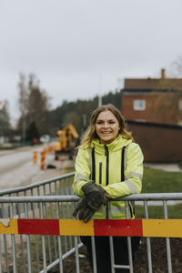 Smiling female road worker leaning against traffic barrier
