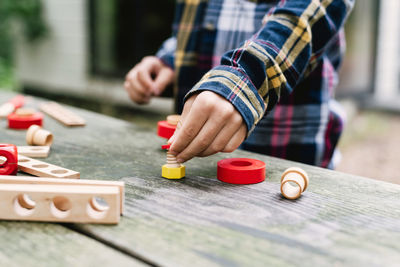 Little boy in a checkered shirt plays with a wooden constructor outdoors.