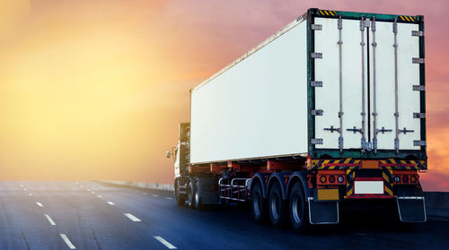 Vehicles on road against sky during sunset