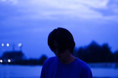 Close-up of young man standing against cloudy sky at dusk