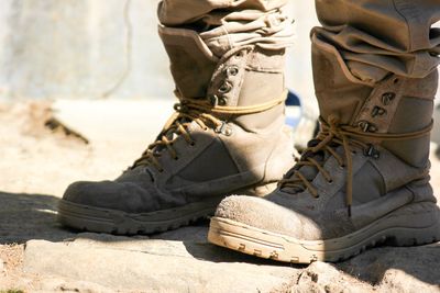 Low section of man wearing boots while standing on footpath during sunny day