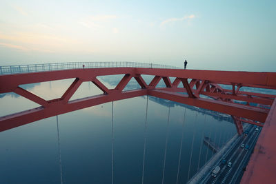 Man standing on railing over river against sky