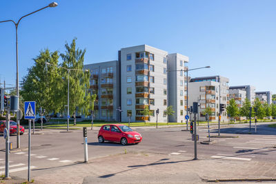 Vehicles on road by buildings against clear sky