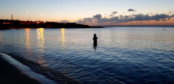 Silhouette man in sea against sky during sunset