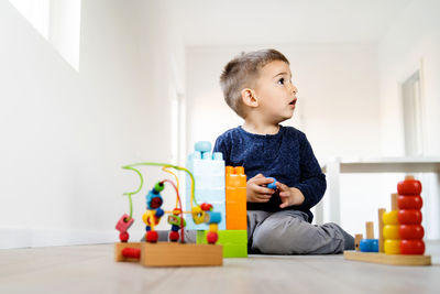 Cute boy looking away while playing on floor at home