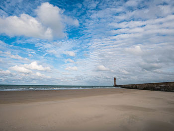 Pier at the beach leading towards lighthouse in the distance