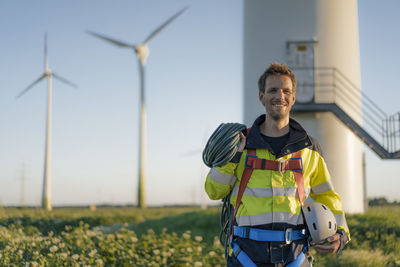 Portrait of smiling technician standing at a wind farm with climbing equipment