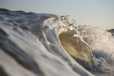 Waves splashing in sea against clear sky during sunset