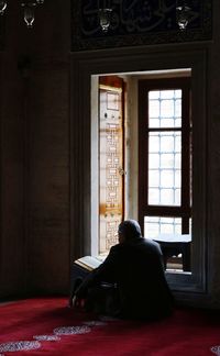 Rear view of man looking through window at home