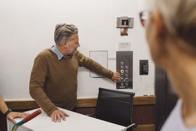 Mature businessman pressing elevator button while moving into new office