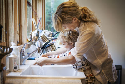 Mother assisting son in washing hands at kitchen sink