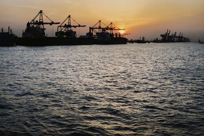 Silhouette cranes at commercial dock against sky during sunset