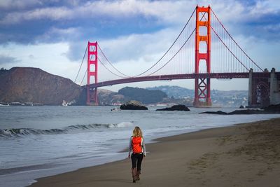Rear view of backpack woman walking at beach near golden gate bridge