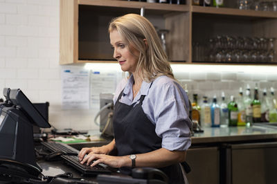 Female owner using computer while standing in cafeteria