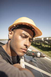 Focused male engineer wearing hardhat and examining solar panels at power station