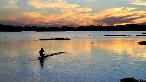 Silhouette man in lake against sky during sunset