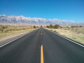 Street amidst grassy field by mountains against blue sky