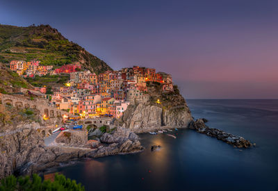 Illuminated manarola town by sea against sky during sunset