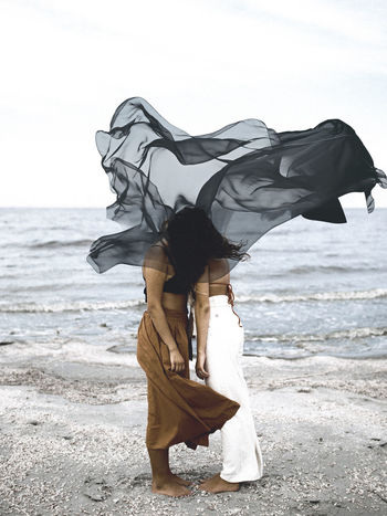 WOMAN STANDING ON BEACH AGAINST SEA