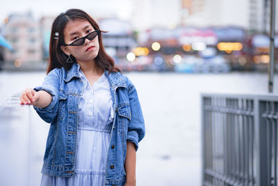 Young woman looking away while standing on railing in city