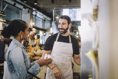 Smiling mature salesman discussing over product with female customer at delicatessen