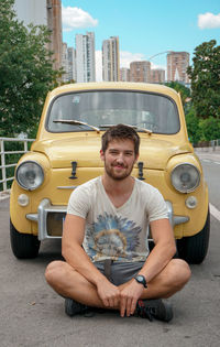 Portrait of smiling young man sitting on road against car