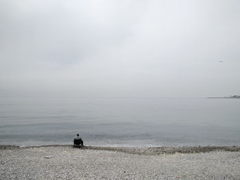 Man fishing at sea shore against sky