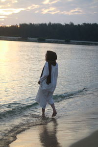 Rear view of woman standing on beach during sunset