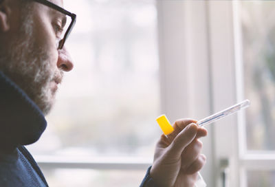 Close-up of man holding thermometer by window