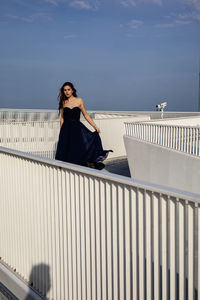 Woman sitting on railing against sky