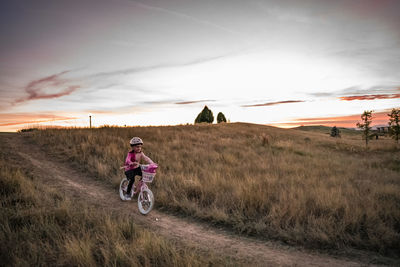 Young girl bikes down a grassy hill at sunset