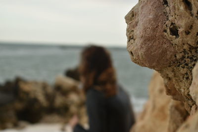 Rear view of woman standing on rock by sea