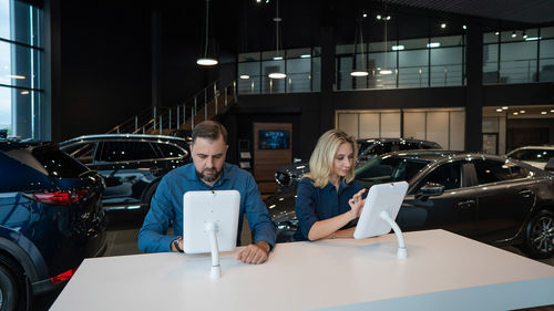 Caucasian married couple chooses a car in a car dealership on digital tablets