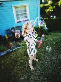 Full length of smiling girl playing with bubbles at backyard