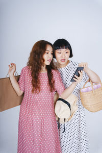 Lesbian couple using smart phone while holding bags against gray background