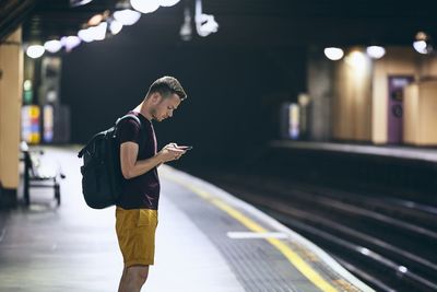 Side view of man using mobile phone at railroad station