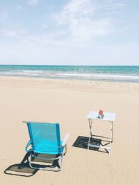 Deck chair and table on beach against sky