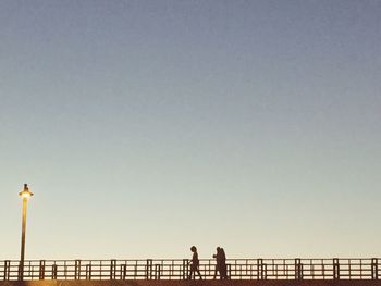 Silhouette man standing by railing against clear sky