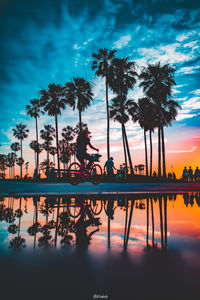 Silhouette palm trees by swimming pool against sky during sunset