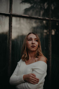 Beautiful young woman looking away while standing against window