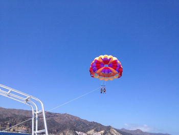 Low angle view of people paragliding against clear blue sky