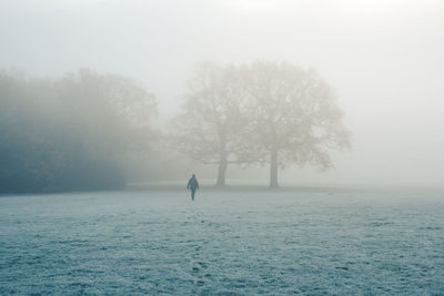 Man standing in the fog on frost covered land against sky at dawn 