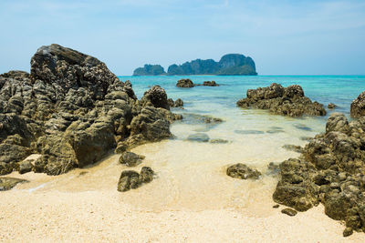 Tropical sea landscape with rocks at sand beach and rocky island at horizon