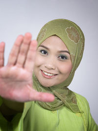 Portrait of cheerful woman in green hijab showing stop gesture against white background