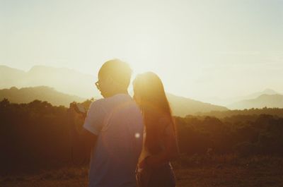 Couple using camera while standing on field during sunset