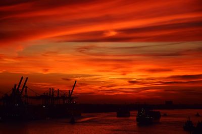 Silhouette sailboats on harbor against dramatic sky during sunset