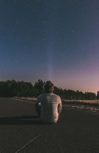 Rear view of man sitting on field against sky at night