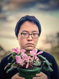 Close-up portrait of young man with pink flowering cyclamen plant.