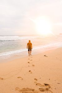 Rear view of boy on beach against sky during sunset